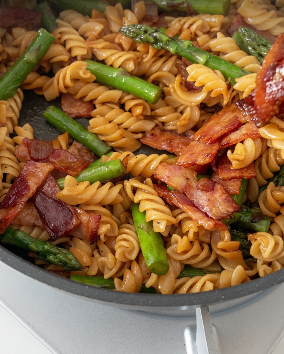 Fusilli, pancetta e asparagi mescolati con la salsa in una padella.