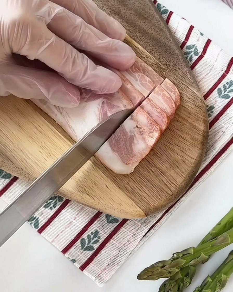 Fette di pancetta cruda tagliate in piccoli cubetti uniformi su un tagliere di legno.