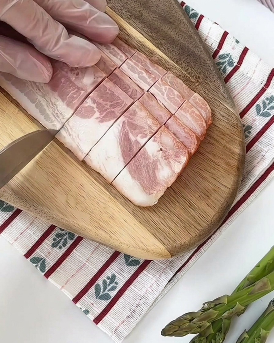 Gambi di asparagi freschi tagliati in segmenti di uguale misura su un tagliere di legno.