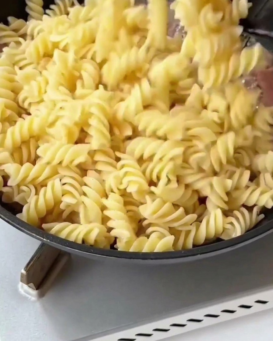 Fusilli cotti e asparagi sbollentati aggiunti in padella con pancetta e cipolla dorate.