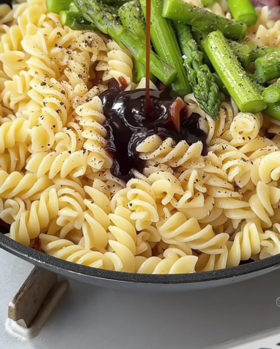 Una salsa scura e saporita versata da un cucchiaio sulla pasta e gli asparagi in padella.