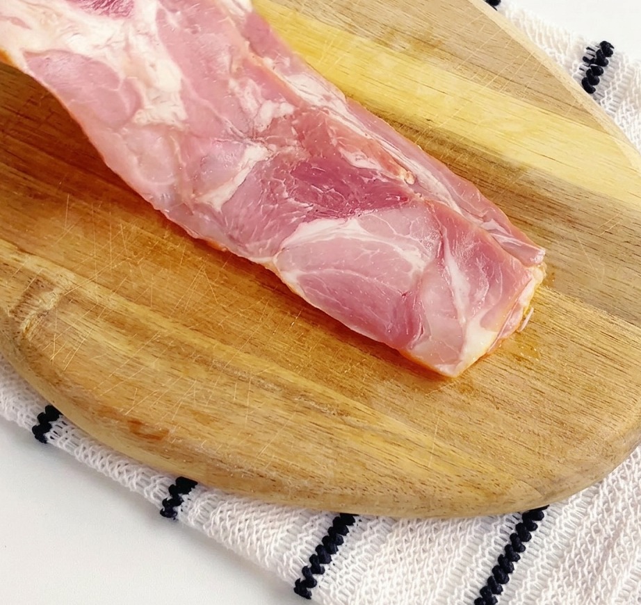 Strisce di pancetta cruda tagliate a piccoli pezzi su un tagliere di legno.