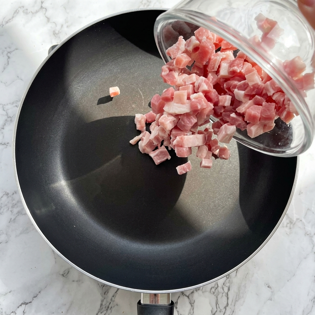 Pancetta a cubetti che soffrigge in padella fino a diventare dorata e croccante.