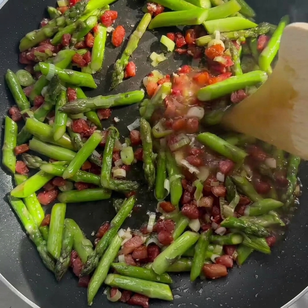 Panna che viene versata sopra il soffritto di pancetta e asparagi in padella.
