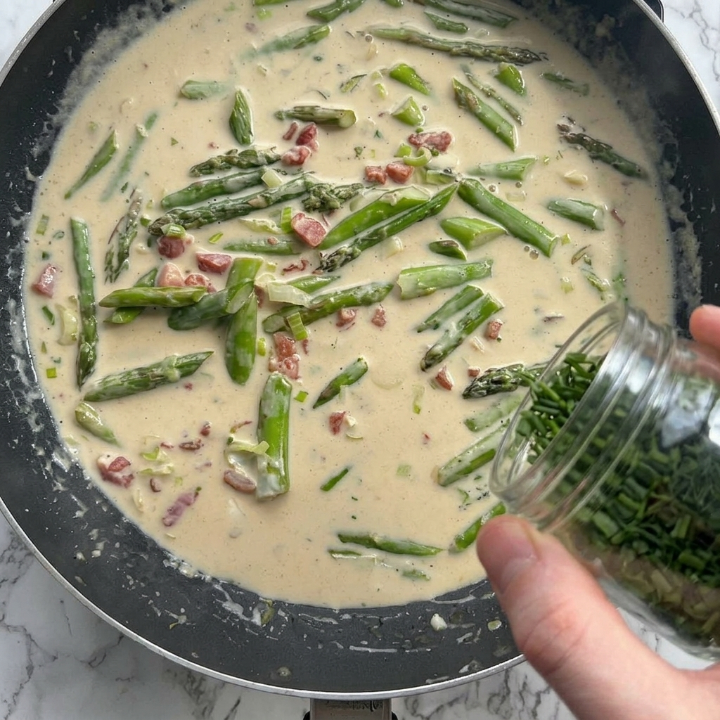 Parmigiano grattugiato ed erbe aromatiche aggiunti alla salsa cremosa in padella.