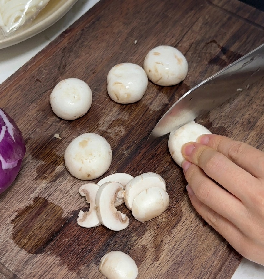 Funghi freschi tagliati a fettine sottili e uniformi su un tagliere di legno.