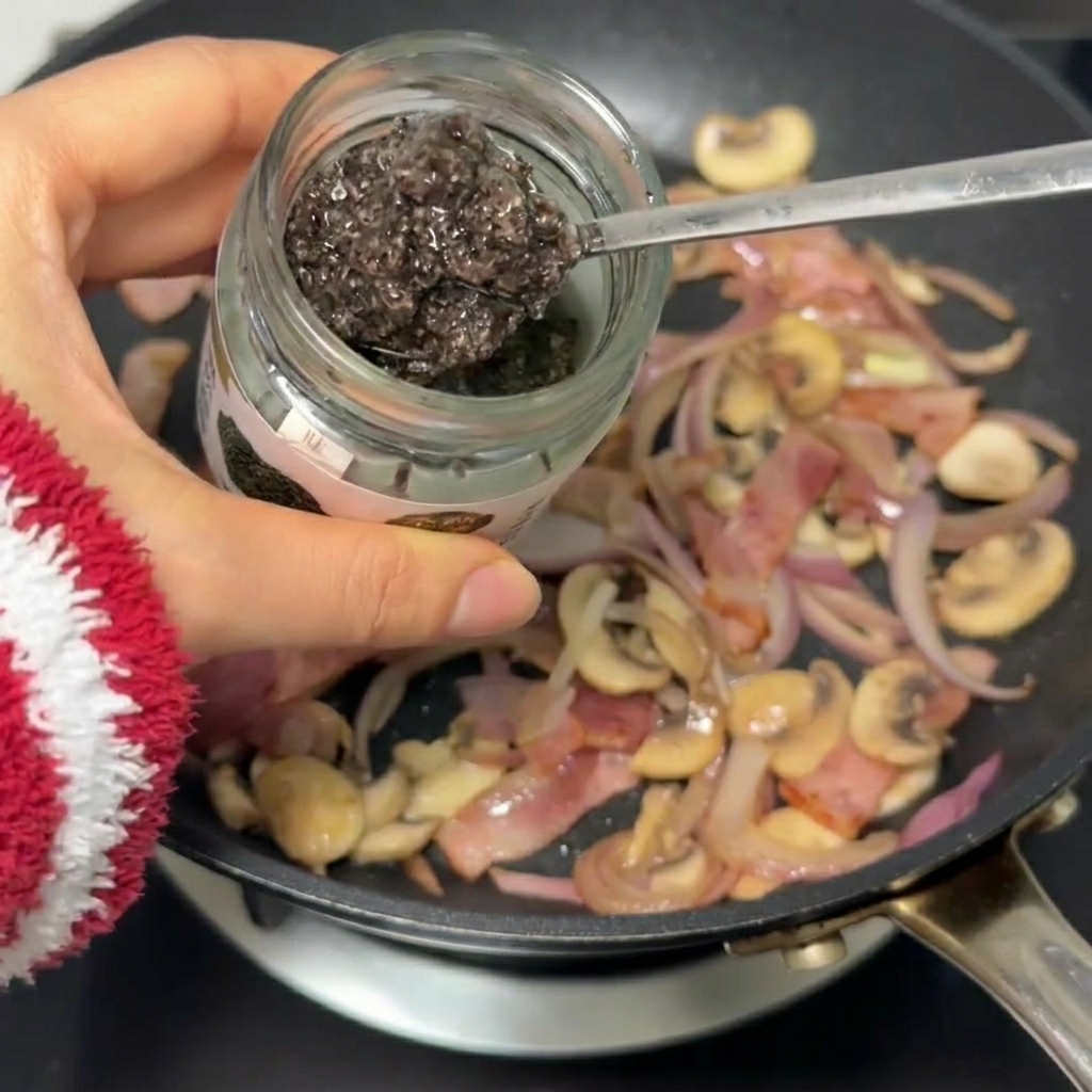 Un cucchiaio di salsa al tartufo scura aggiunta nella padella con bacon, cipolla e funghi.