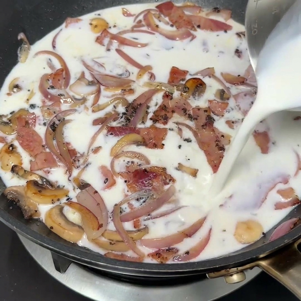 Latte versato in padella insieme al composto di bacon, cipolla e funghi.