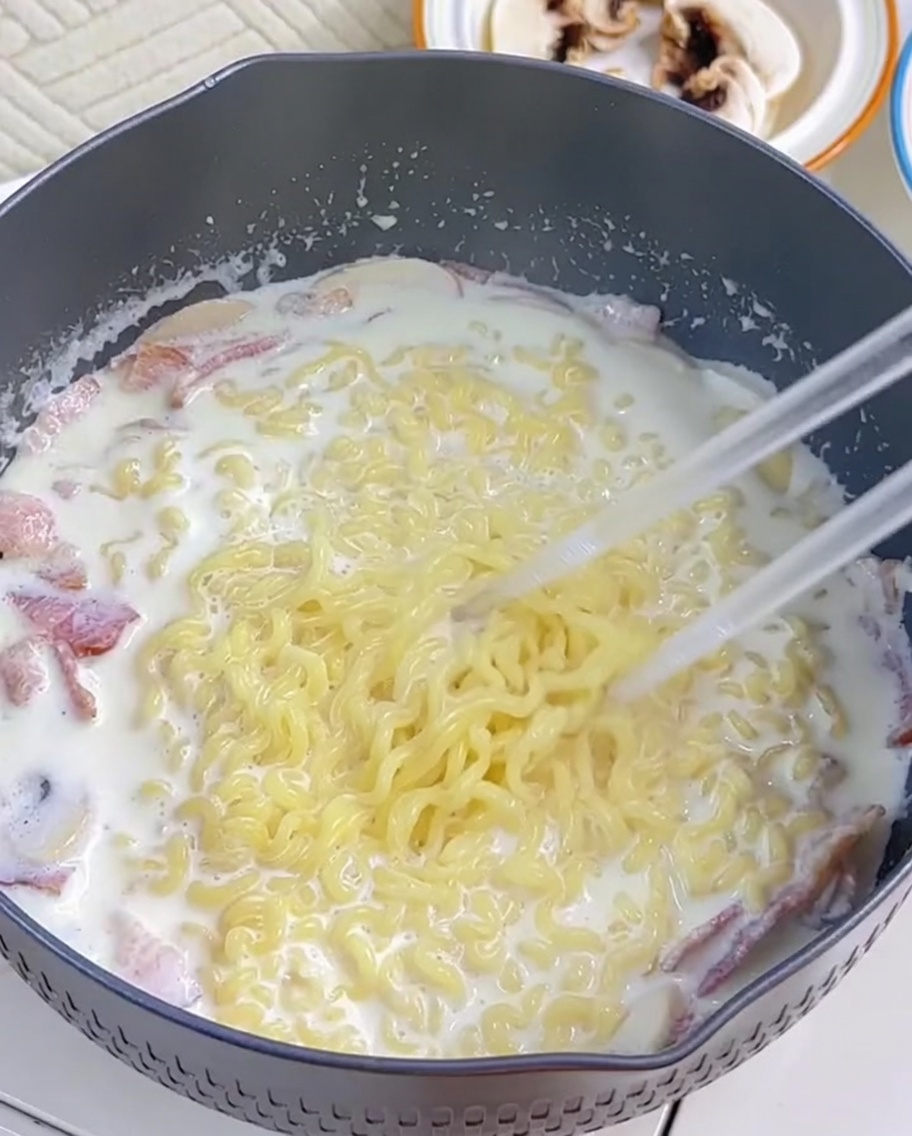 I ramen vengono incorporati nella salsa cremosa usando le bacchette.