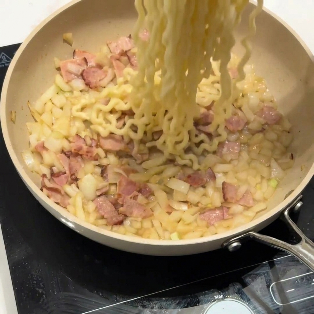 Pasta riccia aggiunta a una padella con pancetta e cipolle.