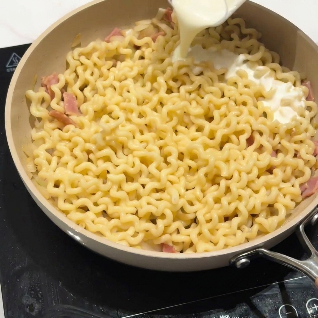 Latte parzialmente scremato versato sulla pasta in padella per creare una salsa.