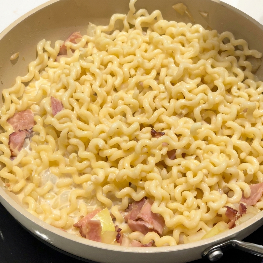 Condimento sparso su pasta riccia e pancetta in una salsa cremosa in padella.