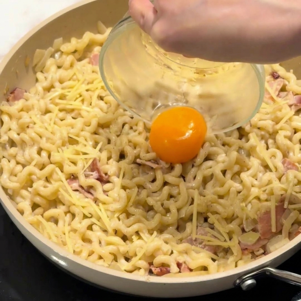Un tuorlo duovo crudo adagiato al centro di un piatto di pasta cremosa in padella.