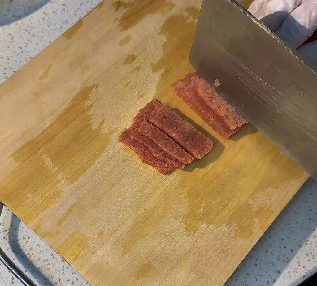 Fette di bacon crudo disposte ordinatamente su un tagliere in legno pronte per essere cucinate.