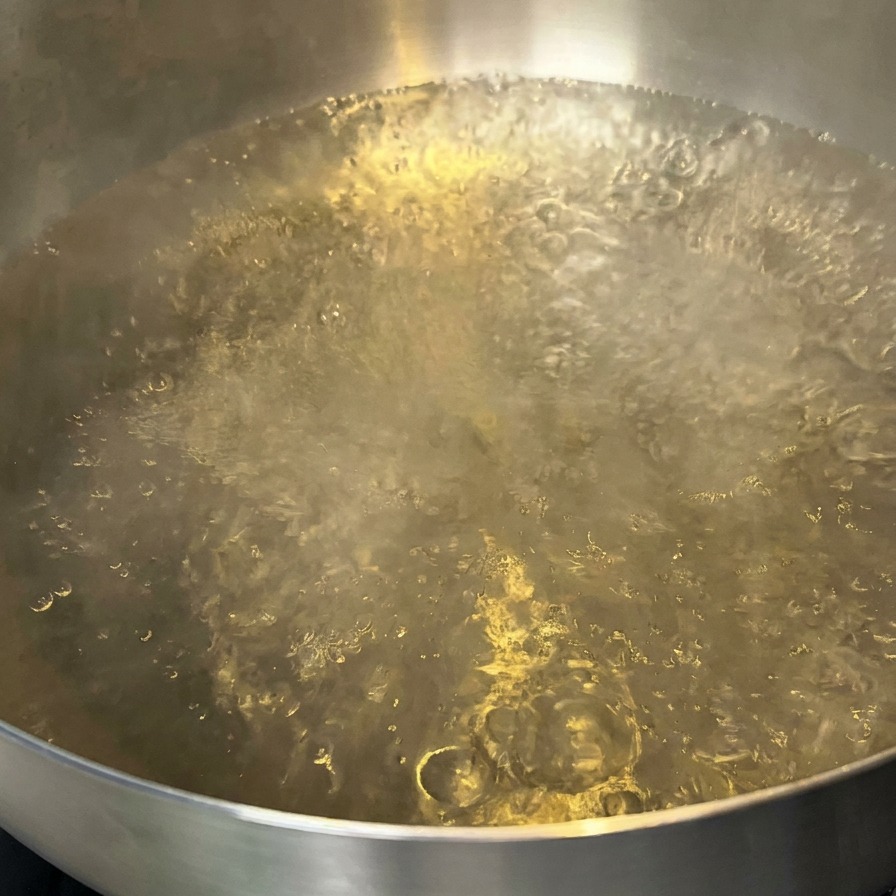 Una pentola dacqua in ebollizione con una piccola quantità di olio che galleggia sulla superficie.