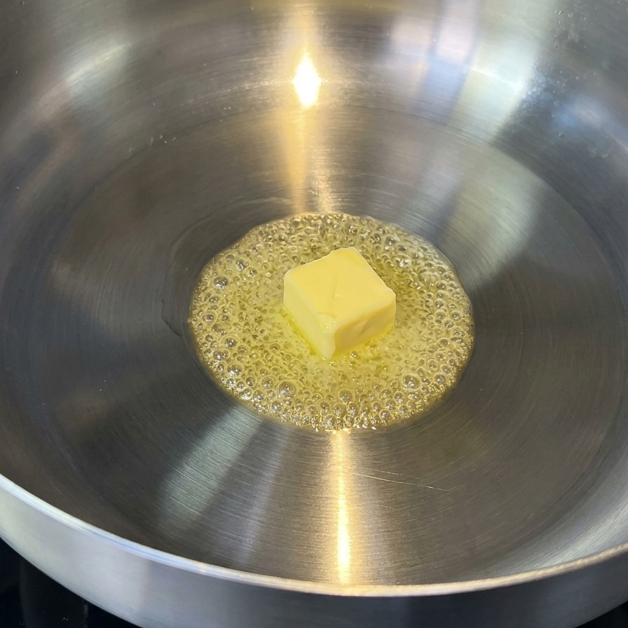 Burro che si scioglie in una padella in acciaio inox, creando bolle dorate.