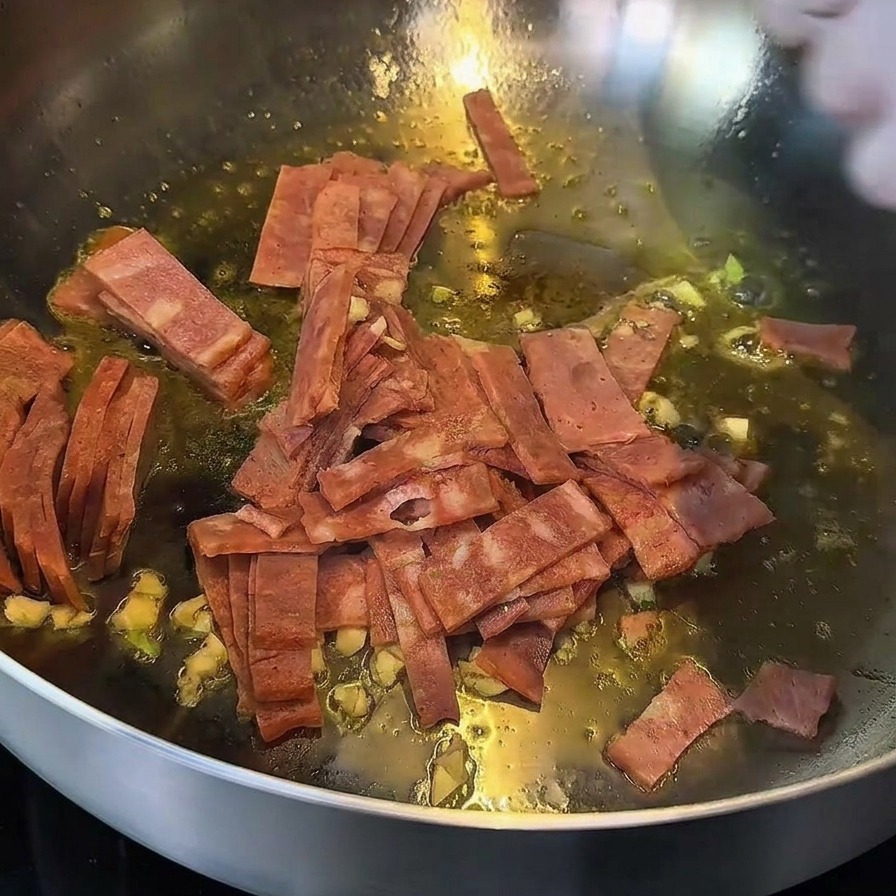 Bacon e aglio che soffriggono in padella, con i bordi del bacon che appaiono dorati.