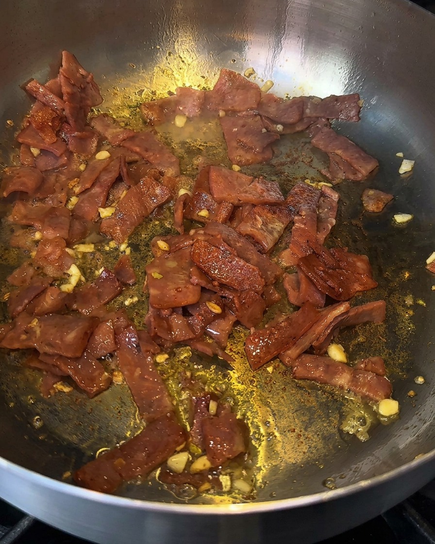 Bacon e aglio sfrigolanti in padella mentre vengono sfumati con un goccio di liquore da cucina.