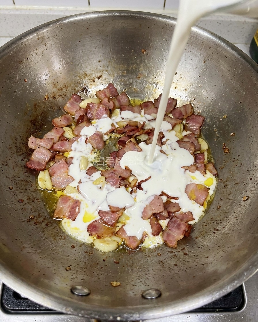 Panna fresca versata nella padella contenente i pezzi di bacon e aglio.