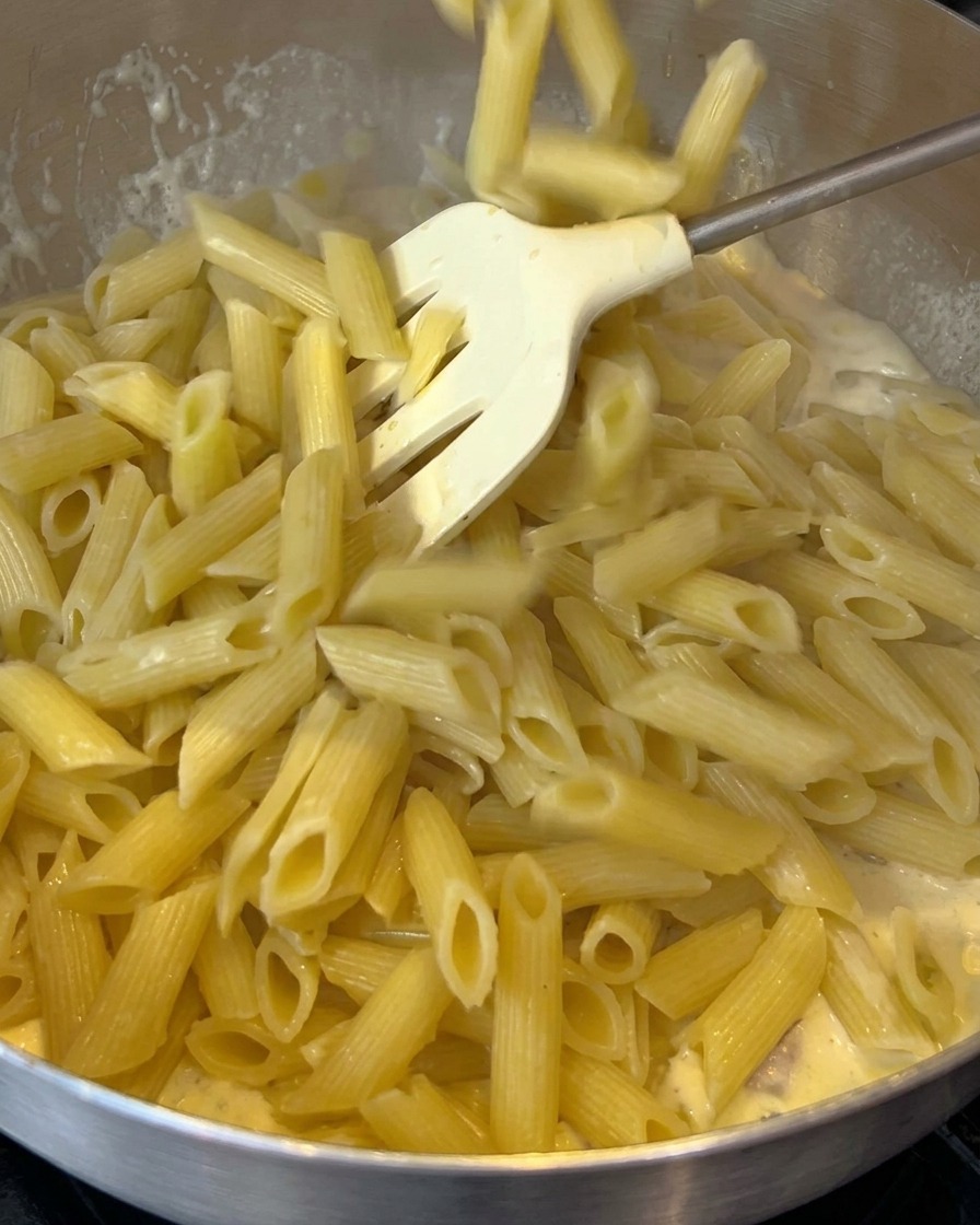 Penne cotte aggiunte in una padella con una salsa cremosa al bacon.