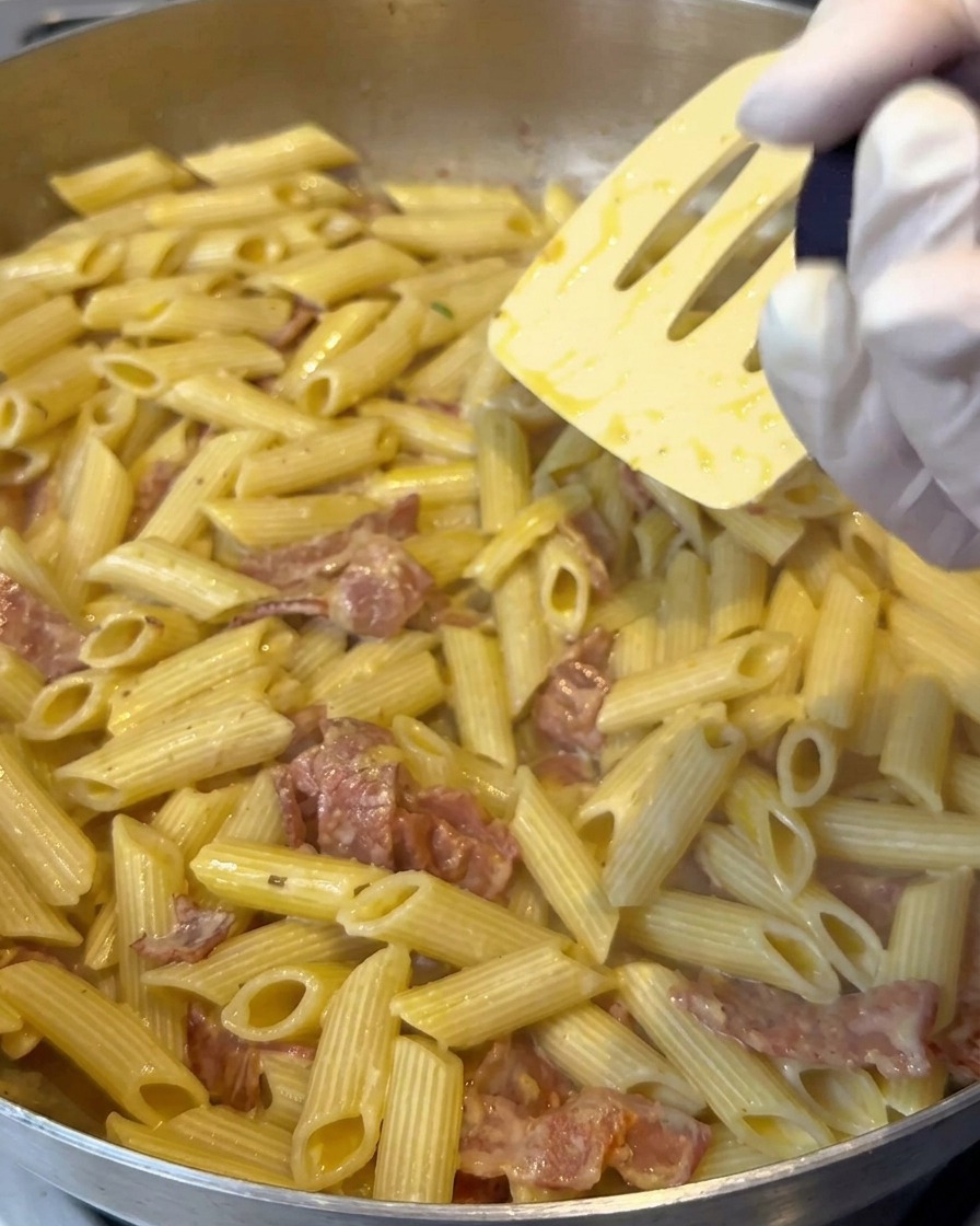 Sale al limone grattugiato su una padella di penne cremose mentre vengono mescolate.