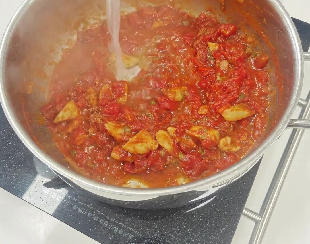 Un vivace sugo di pomodoro rosso che sobbolle in padella, con pezzetti visibili di pomodori secchi e capperi.