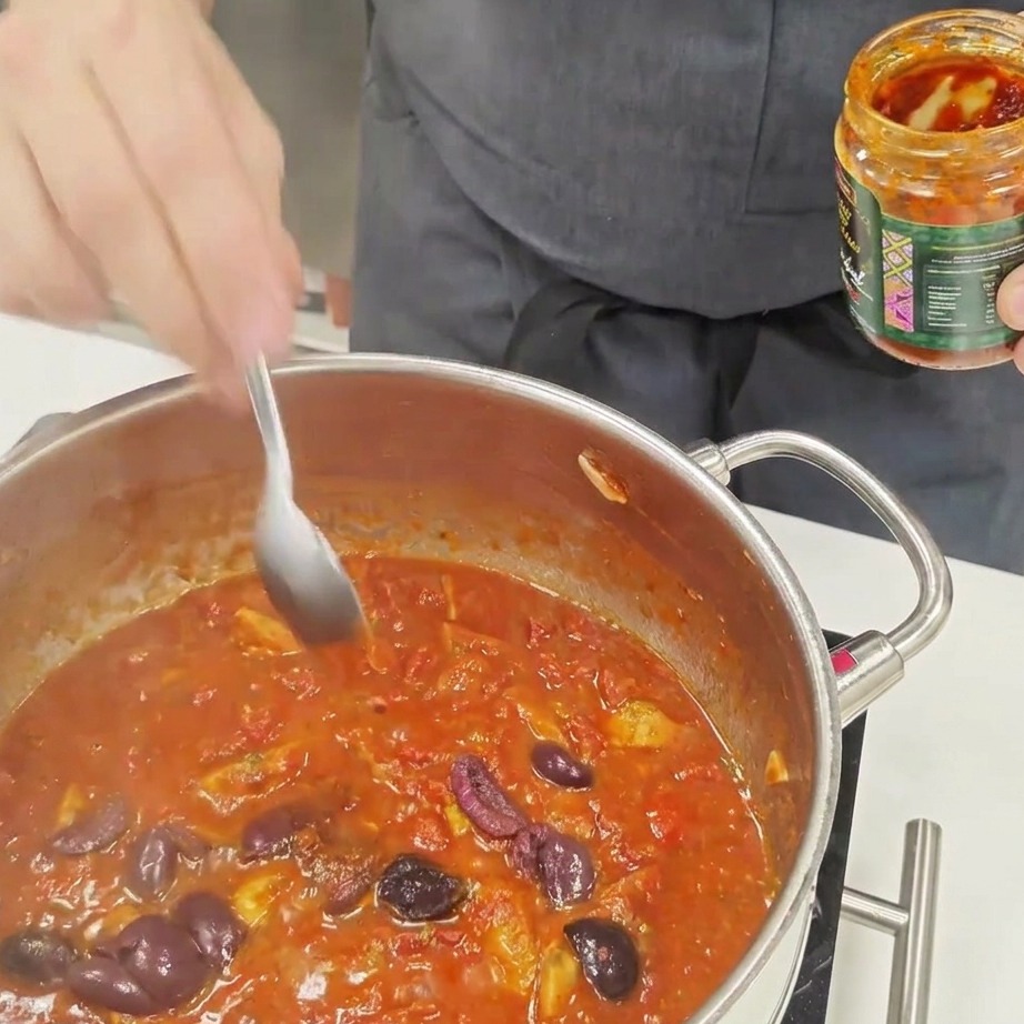 Un cucchiaio di salsa piccante mescolato in un sugo di pomodoro in ebollizione.