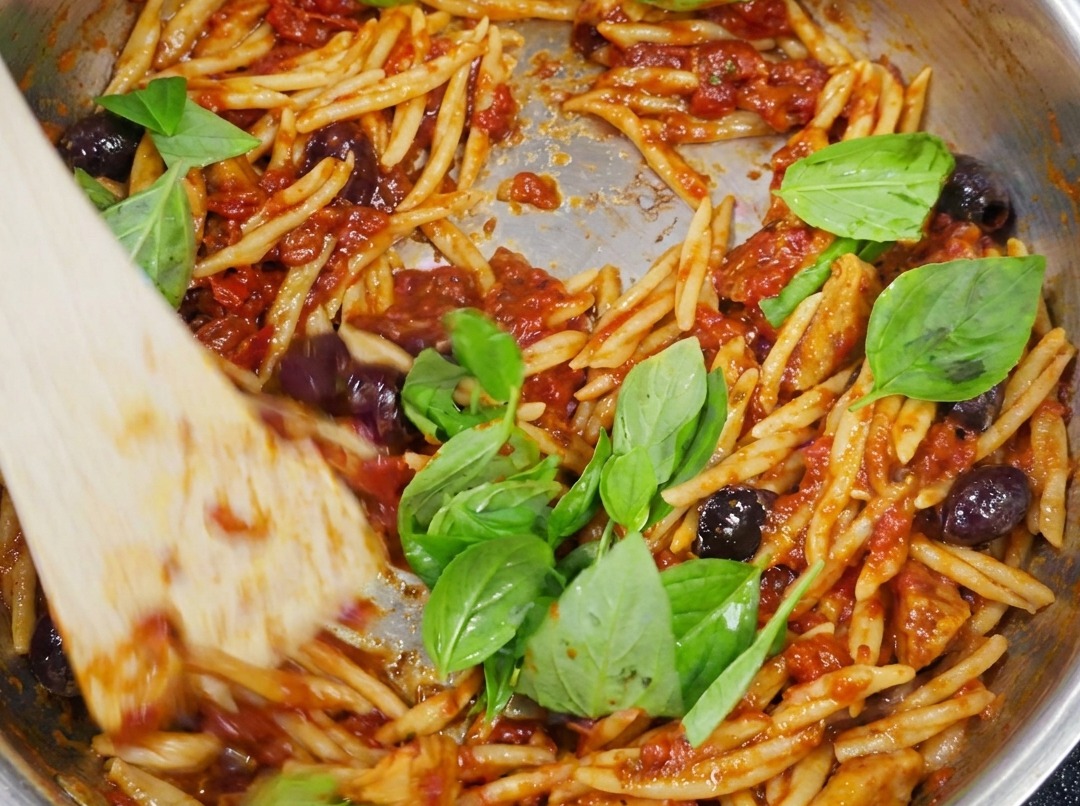 Trofie pronte condite con sugo alla puttanesca e guarnite con foglie di basilico fresco e verde.