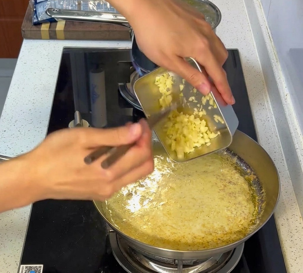 Aglio tritato mescolato in una salsa bianca cremosa in una padella di acciaio inossidabile.