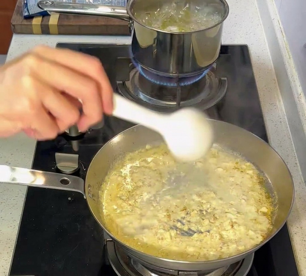 Pinze che trasferiscono la pasta al dente da una pentola bollente nella padella con la salsa cremosa.