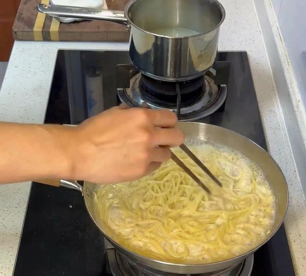 Pasta mescolata con bacchette in una salsa cremosa, avvolgendo ogni singolo spaghetto.