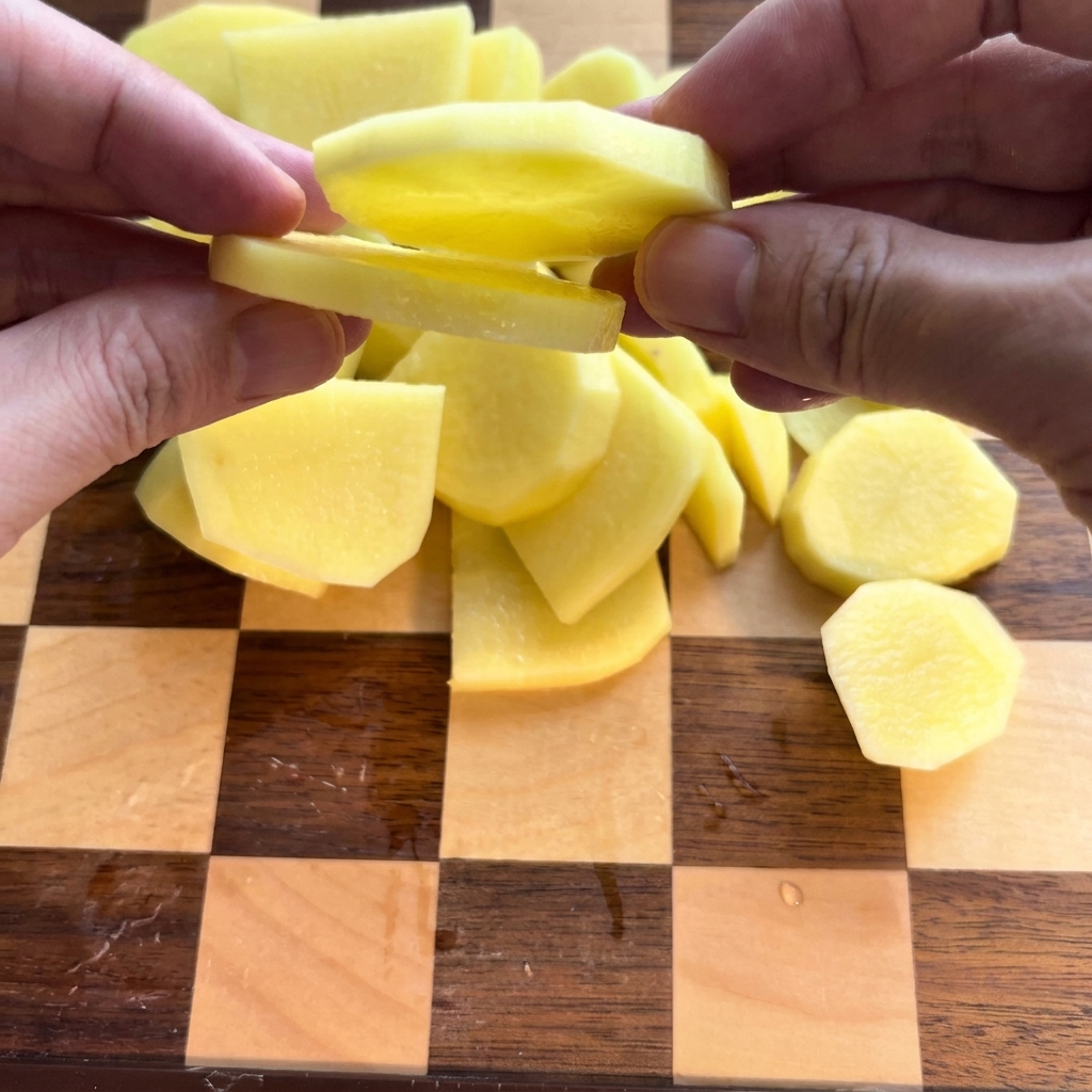 Patate sbucciate tagliate con cura a fette rotonde su un tagliere di legno.