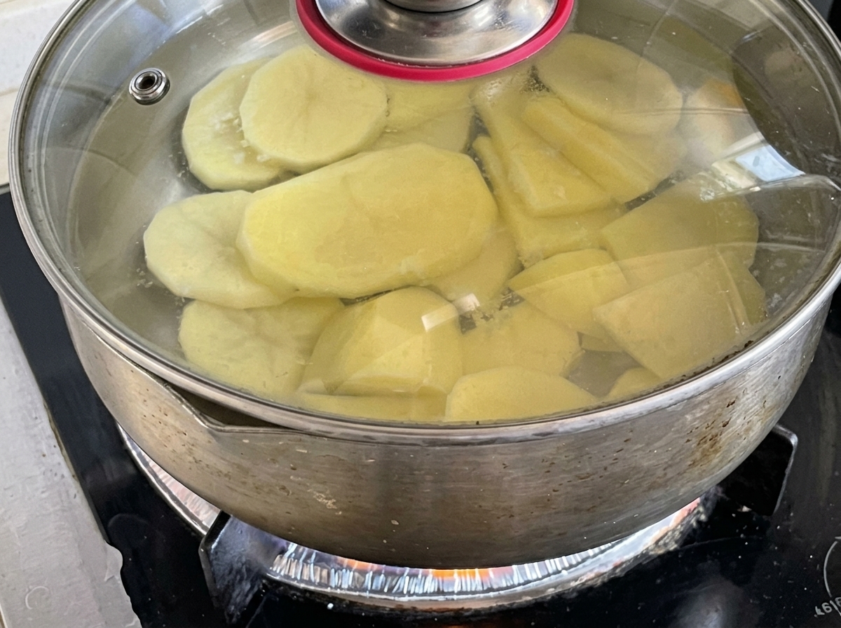 Fette di patate che sobbollono in una pentola dacqua coperta sui fornelli.