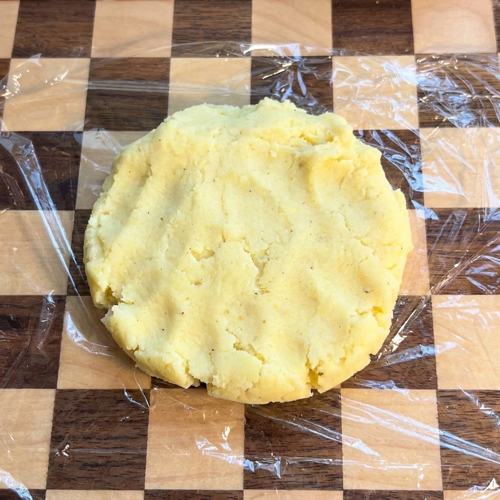Una base circolare di patate su un tagliere coperto da pellicola trasparente.