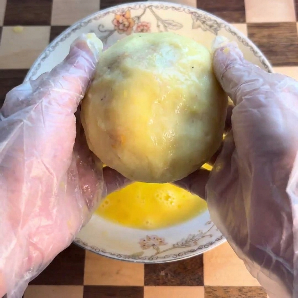 Una polpetta di patate immersa in una ciotola con uovo sbattuto.