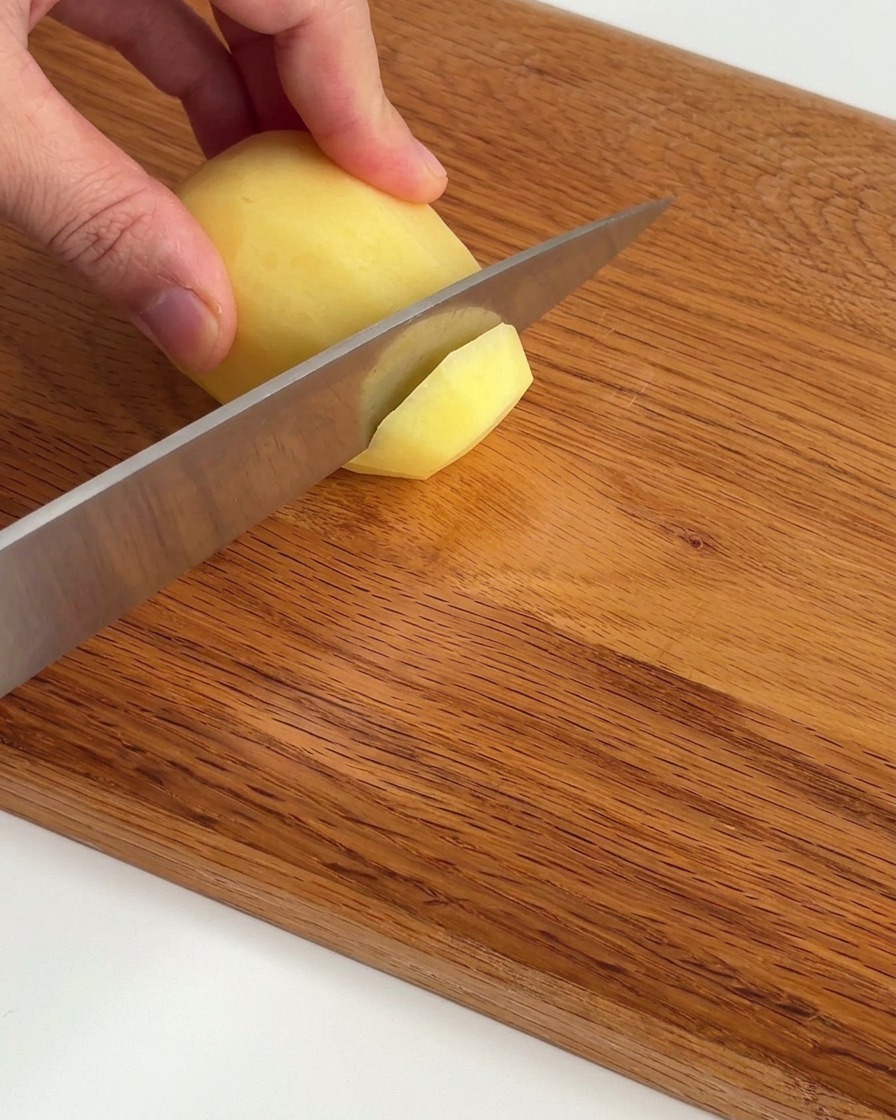 Patate crude affettate sottilmente e disposte in ordine su un tagliere di legno.