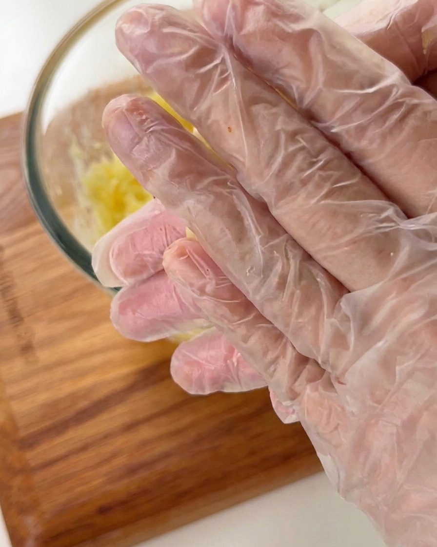 Mani con guanti monouso che modellano la pasta di patate in piccole forme a cestino.