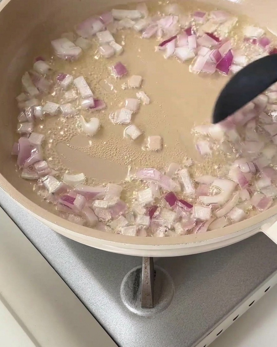Cubetti di cipolla rossa che sfrigolano in padella con olio caldo.