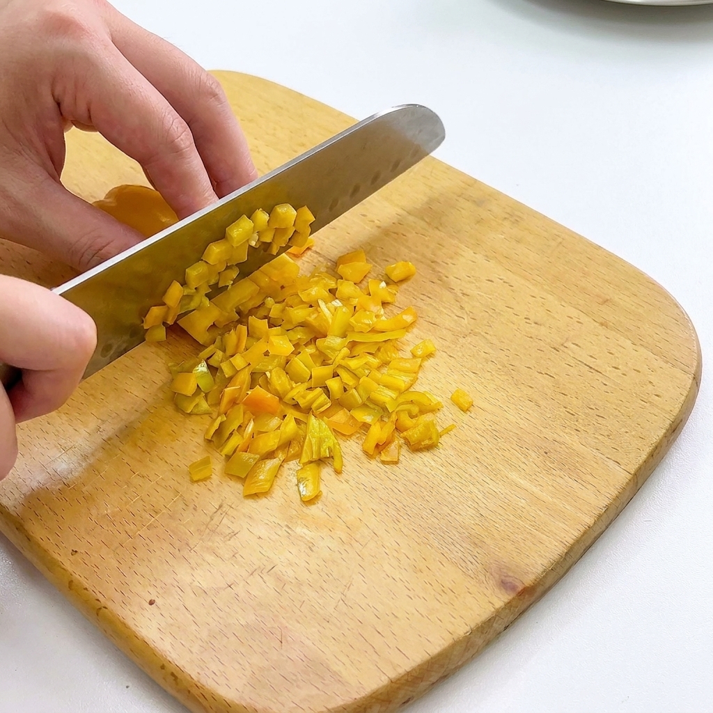 Peperoni e cipolle tagliati a cubetti piccoli su un tagliere di legno.
