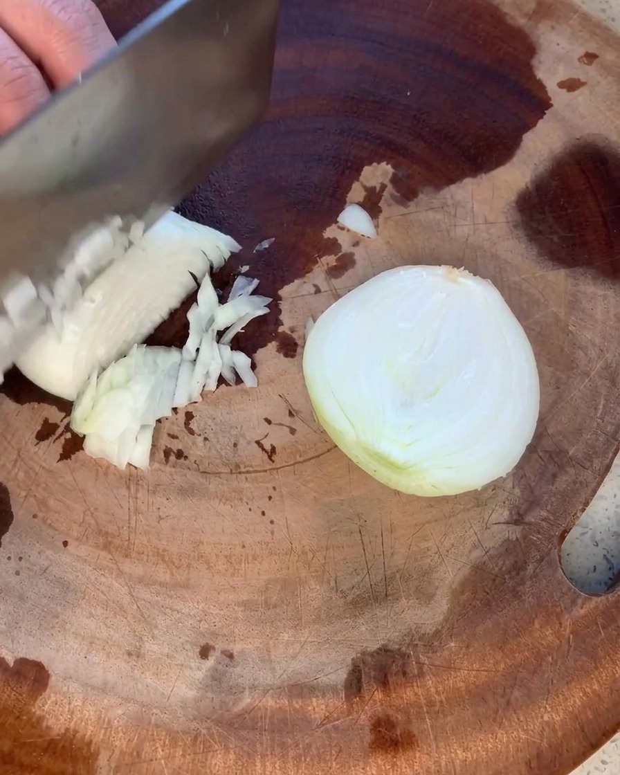 Una cipolla gialla tritata con cura in piccoli pezzi uniformi su un tagliere di legno rustico.