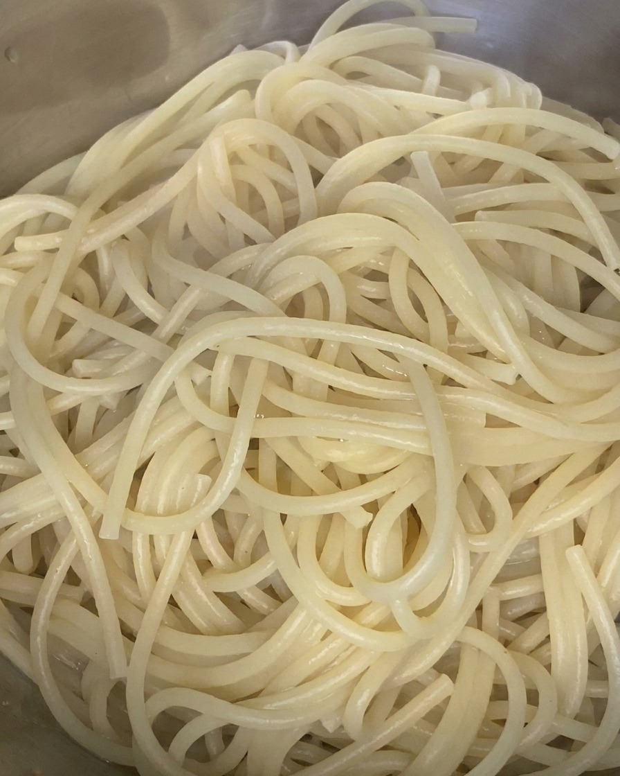 Spaghetti cotti mescolati con un filo dolio doliva in una ciotola di acciaio inox.