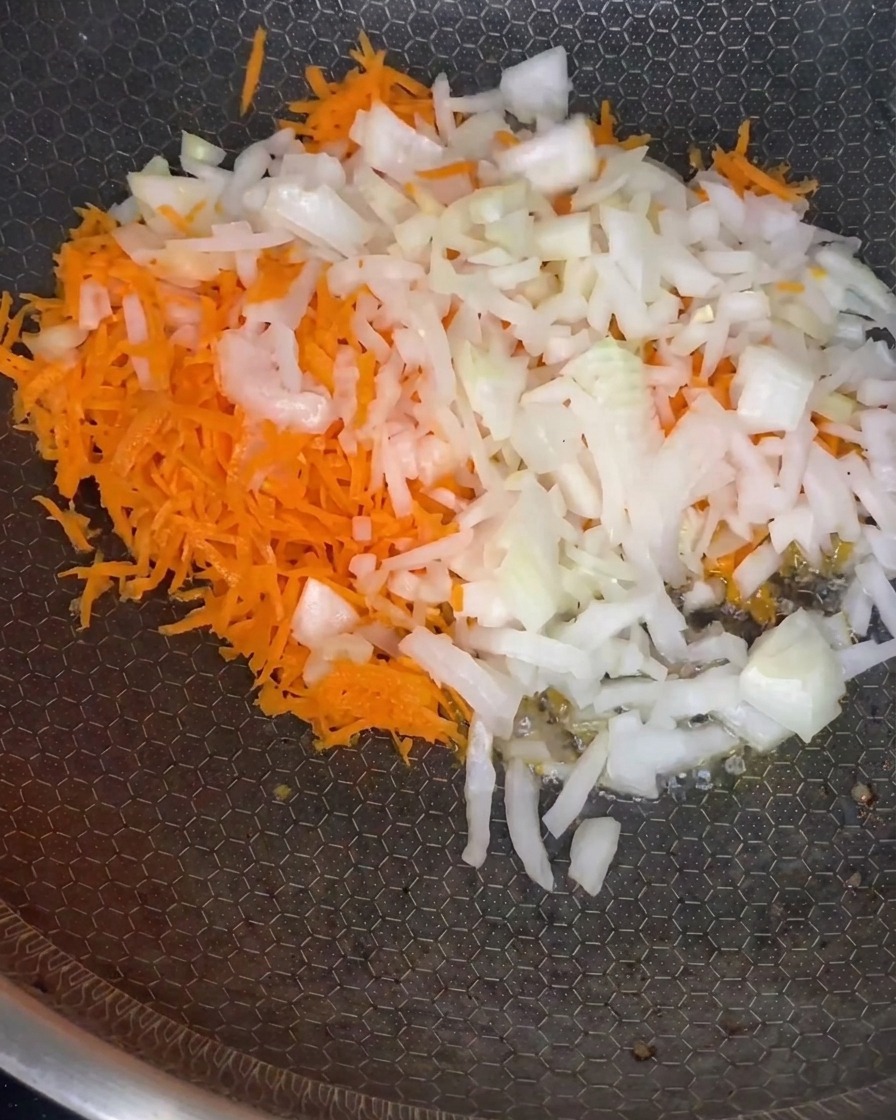 Un mix di carote grattugiate e cipolle tritate che appassiscono in padella a fuoco medio.