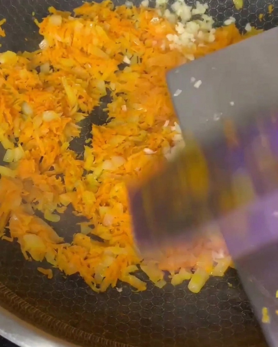 Aglio tritato e spezie italiane incorporate nel mix di carote e cipolle in padella.
