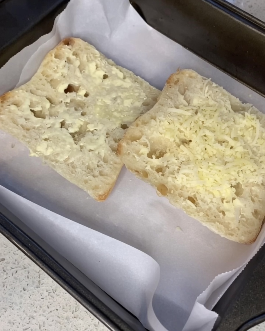 Parmigiano grattugiato cosparso sopra fette di ciabatta imburrate su una teglia.