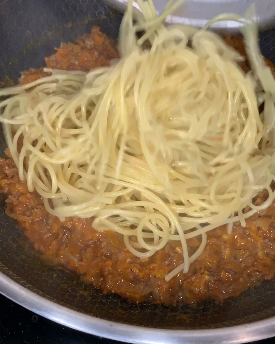 Pasta cotta saltata e mescolata nel ragù ricco e denso in una grande padella.
