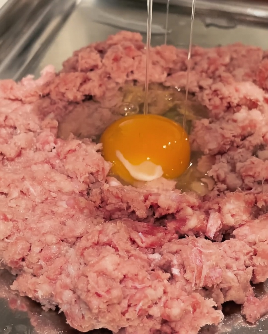 Un uovo crudo rotto in una ciotola con il manzo macinato.