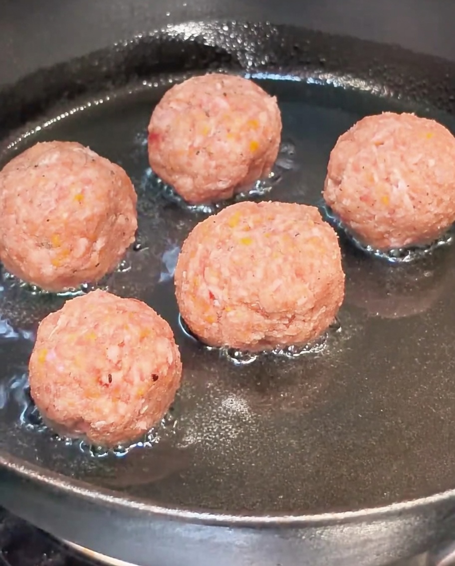 Polpette crude che dorano in una padella oliata.