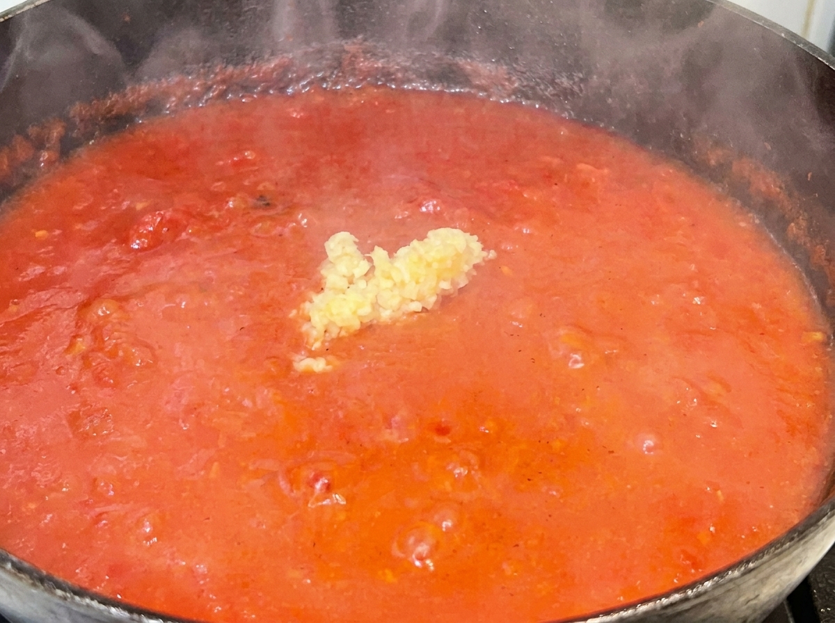Aglio tritato al centro di un sugo rosso in ebollizione.