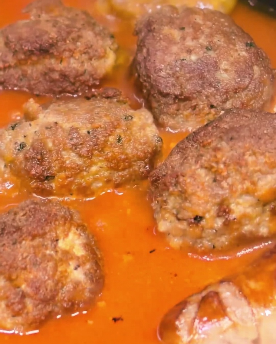 Polpette e salsicce che sobbollono insieme in un sugo rosso denso.