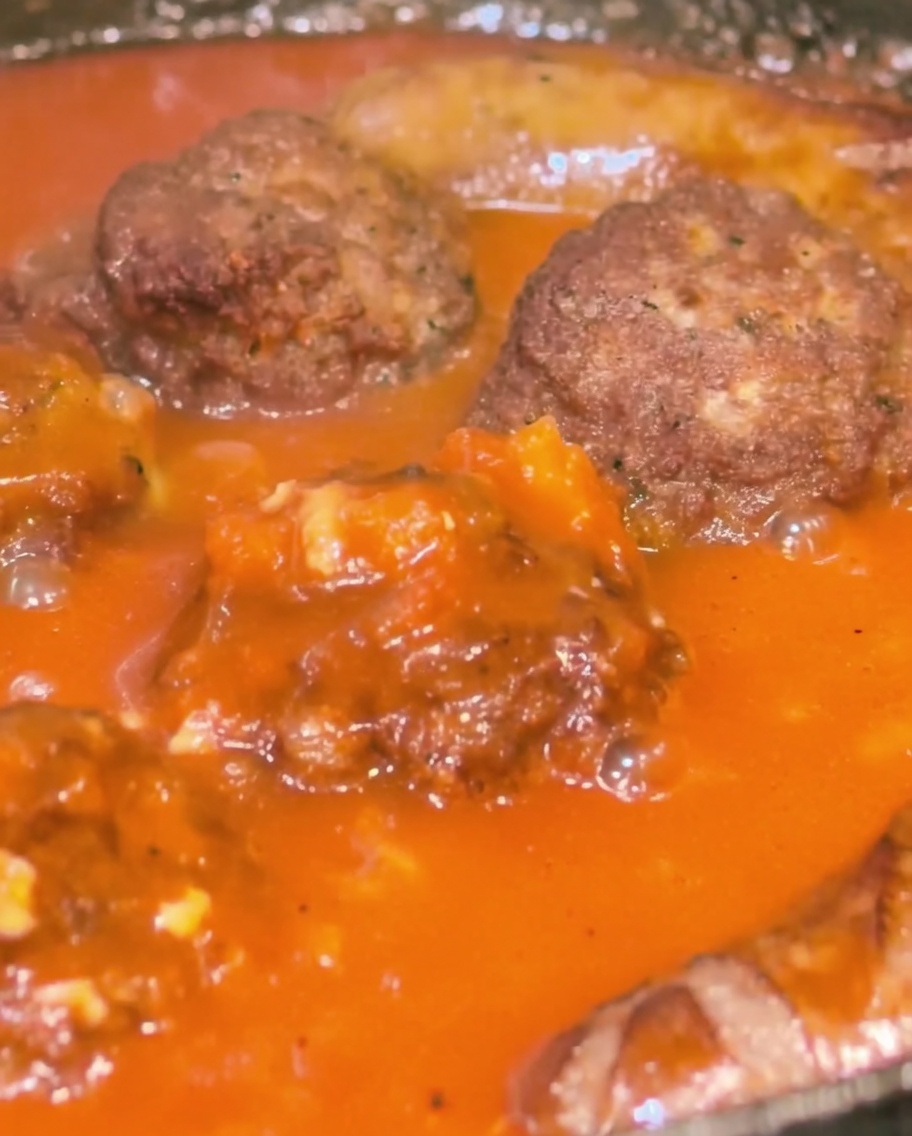 Dettaglio di polpette e salsicce irrorate col sugo in padella.